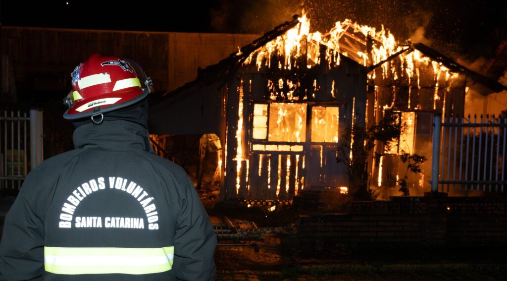 bombeiro observa incêndio em residência de madeira