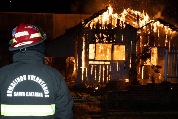 bombeiro observa incêndio em residência de madeira